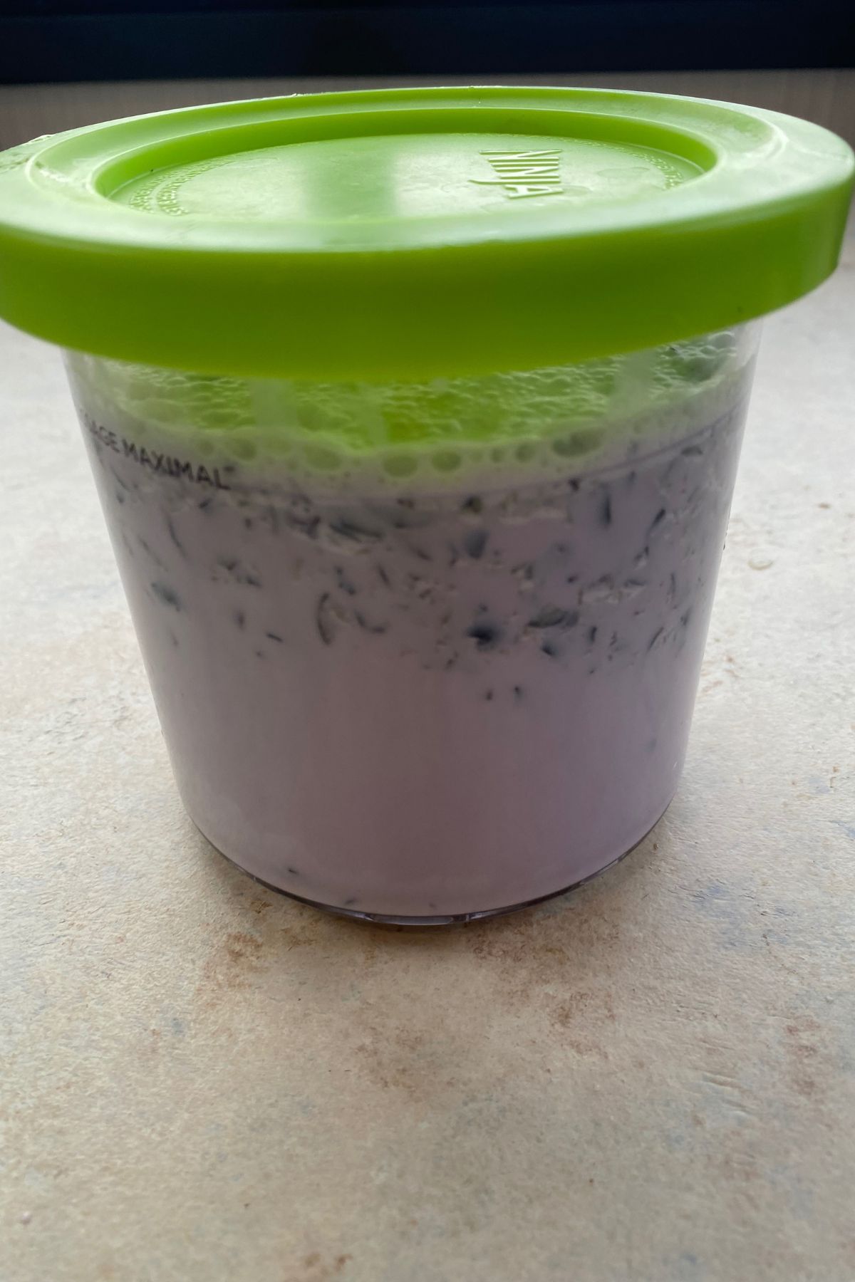 A container of blueberry yogurt with a green lid sitting on a counter.