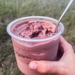 A person holding a cup of cherry chocolate chip ice cream in the middle of a field.