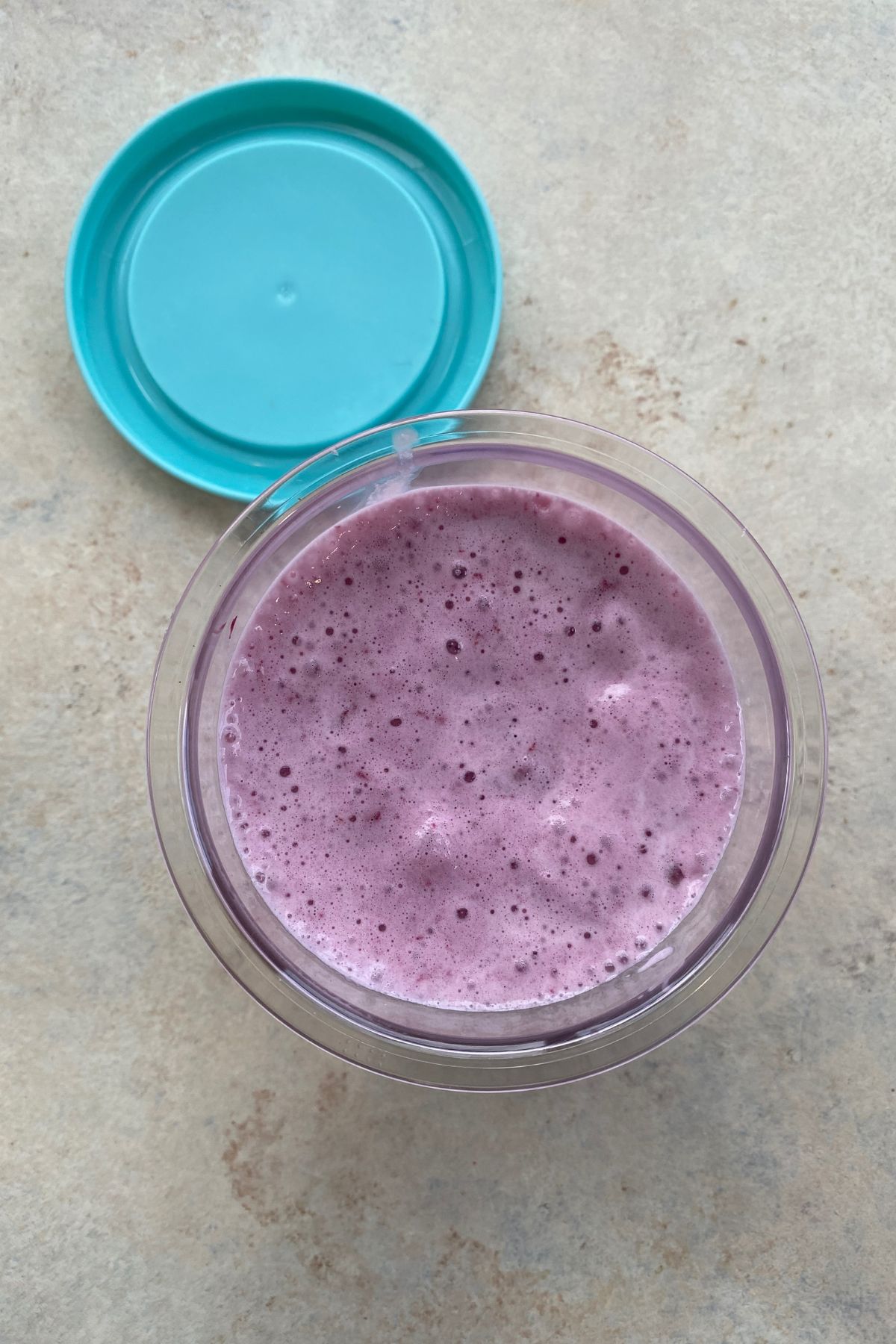 A bowl of blueberry smoothie with a blue lid and a cherry on top.