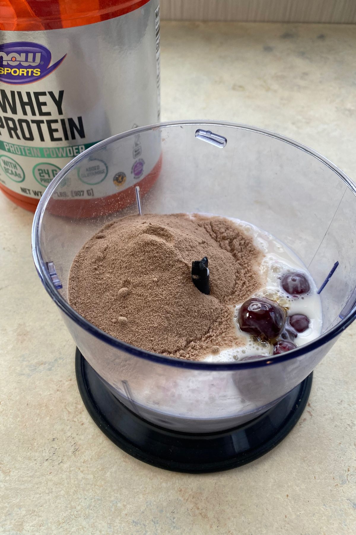 A bowl of chocolate whey protein next to a bowl of cherries.