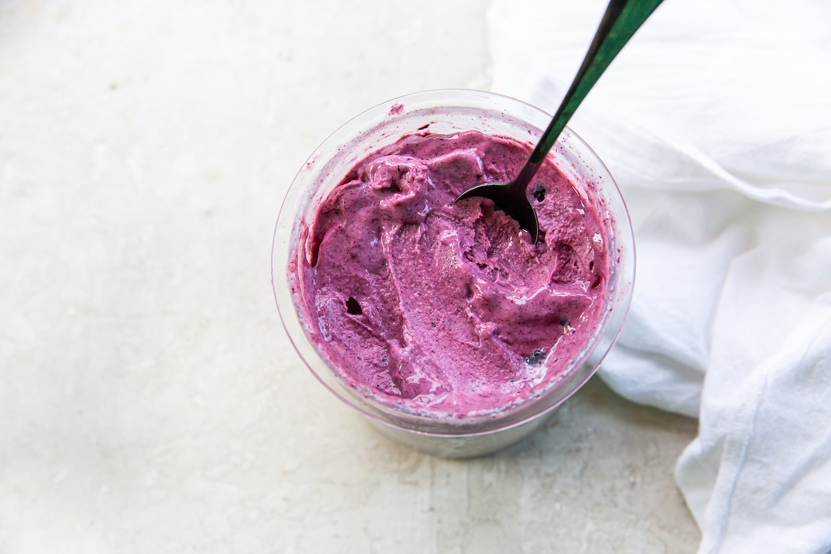 A bowl of freshly scooped blueberry ice cream with a spoon.