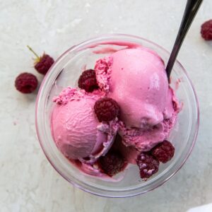 Raspberry ice cream in a bowl with raspberries.