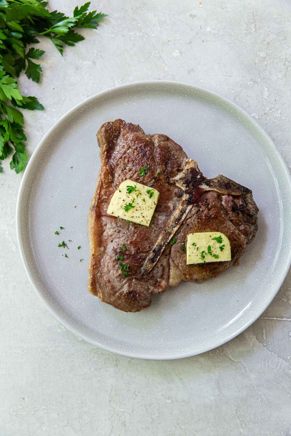 A steak with butter and parsley on a plate.