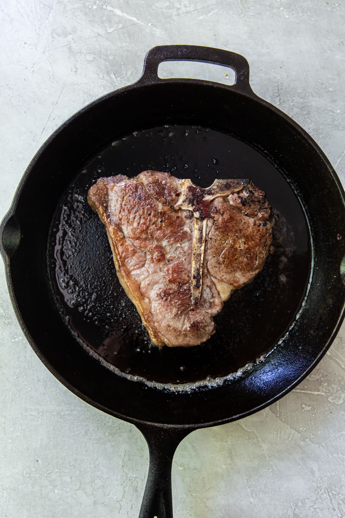 A piece of meat is being cooked in a cast iron skillet.