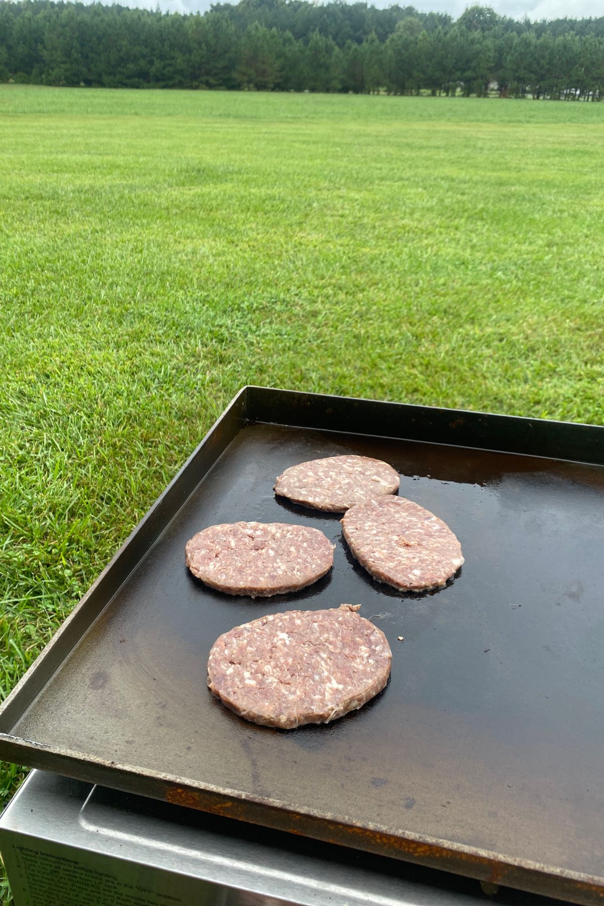 Burgers are being cooked on a grill in a field.