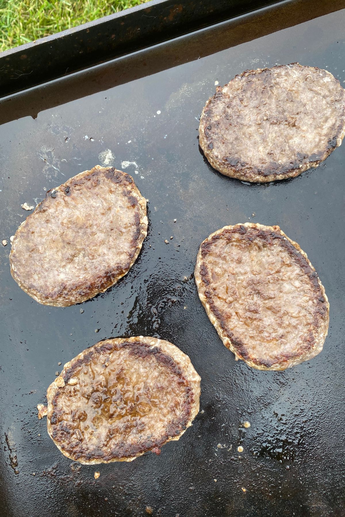 Four hamburger patties are being cooked on a grill.