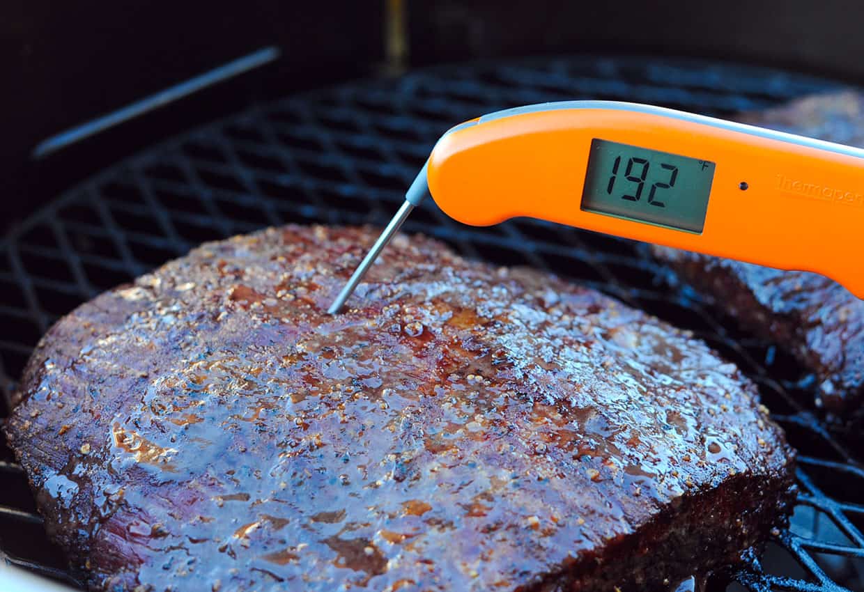 Checking the internal temperature of a meat brisket on a grill with a digital food thermometer.