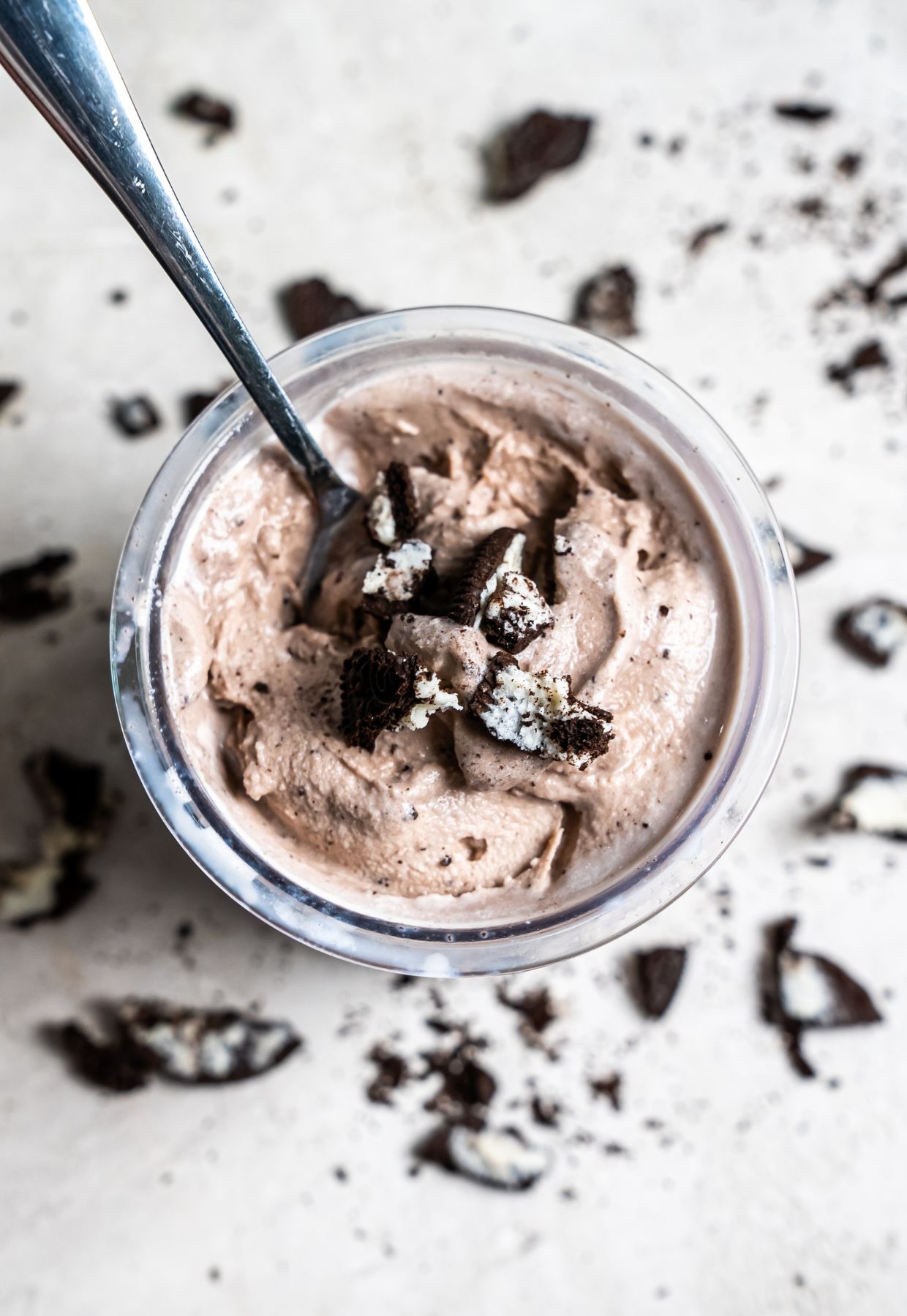 cookies and cream ice cream in a clear pint with Oreos and a spoon.