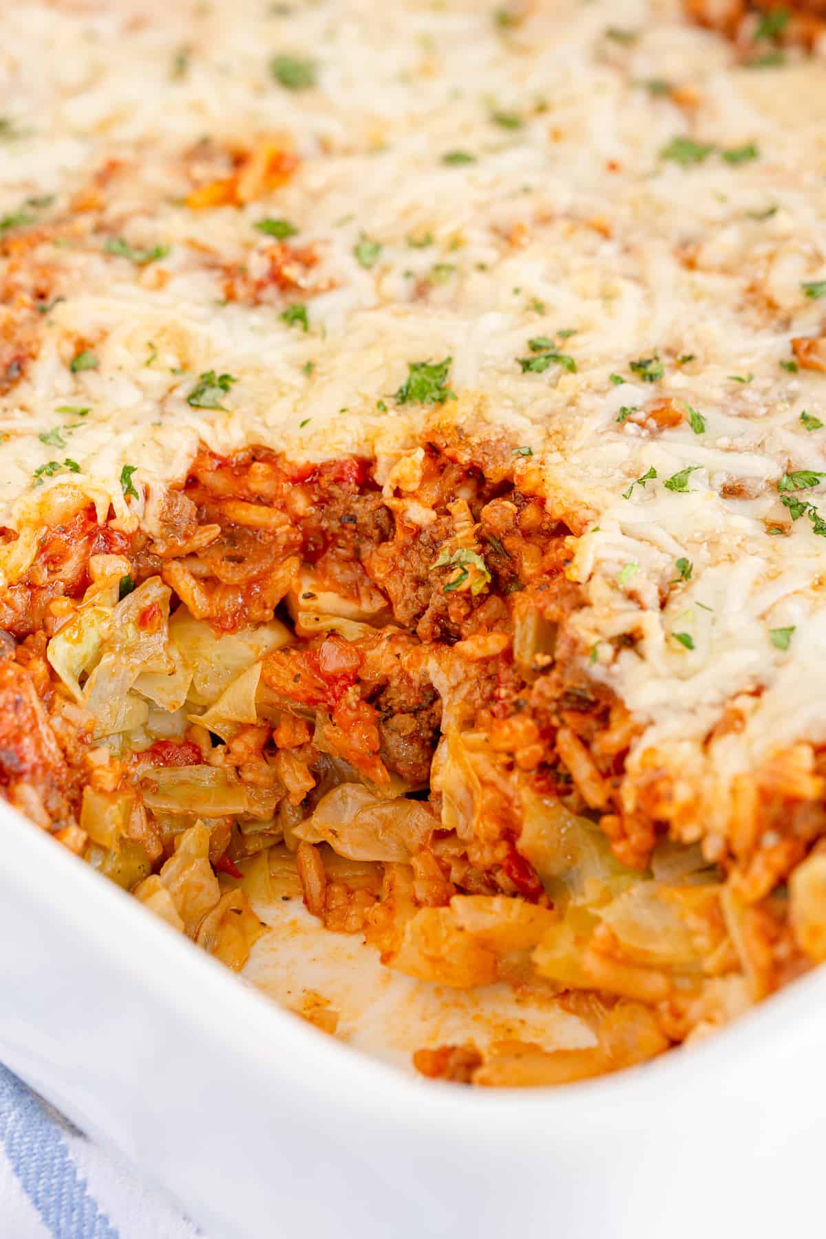 A partially served baked casserole dish with a layer of melted cheese on top, revealing a mixture of cooked ground meat, rice, cabbage, and tomato sauce underneath—a perfect example of the comfort casseroles bring to the table.