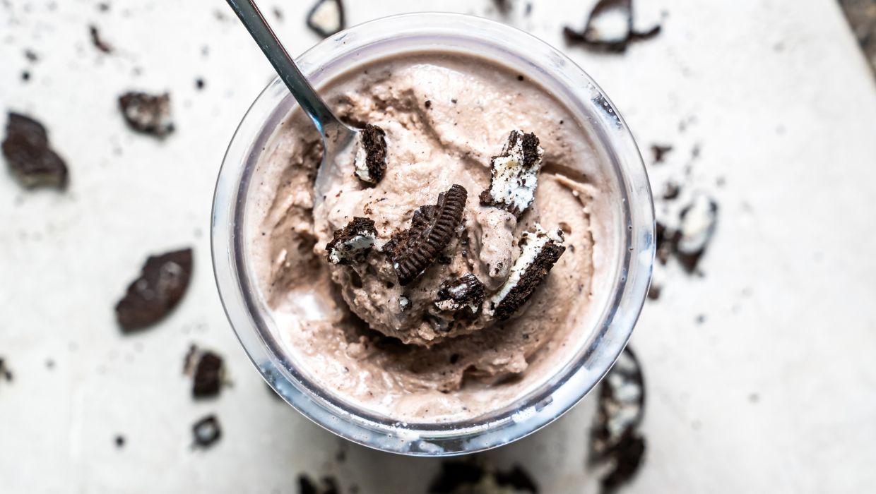 Top view of a cookies and cream milkshake in a glass jar with a straw, topped with cookie chunks on a marble surface.