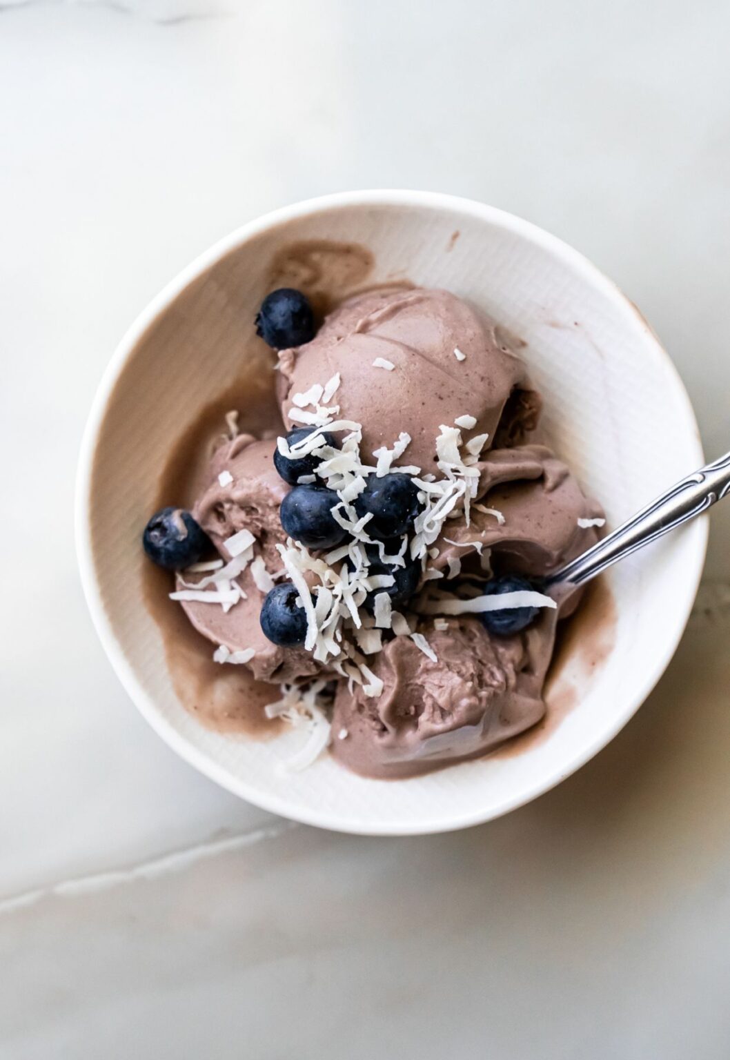 Ninja Creami acai ice cream with a spoon and coconut flakes and blueberries.