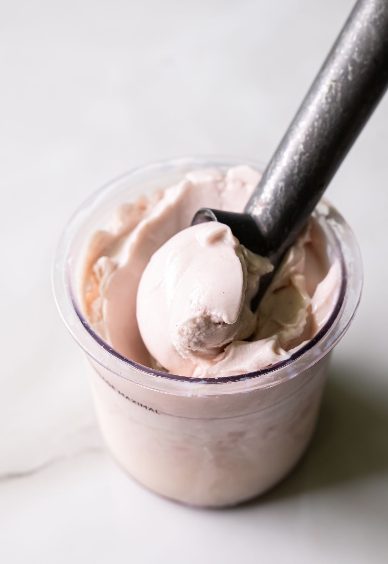 A metal ice cream scoop placed in a container of creamy pink ice cream.