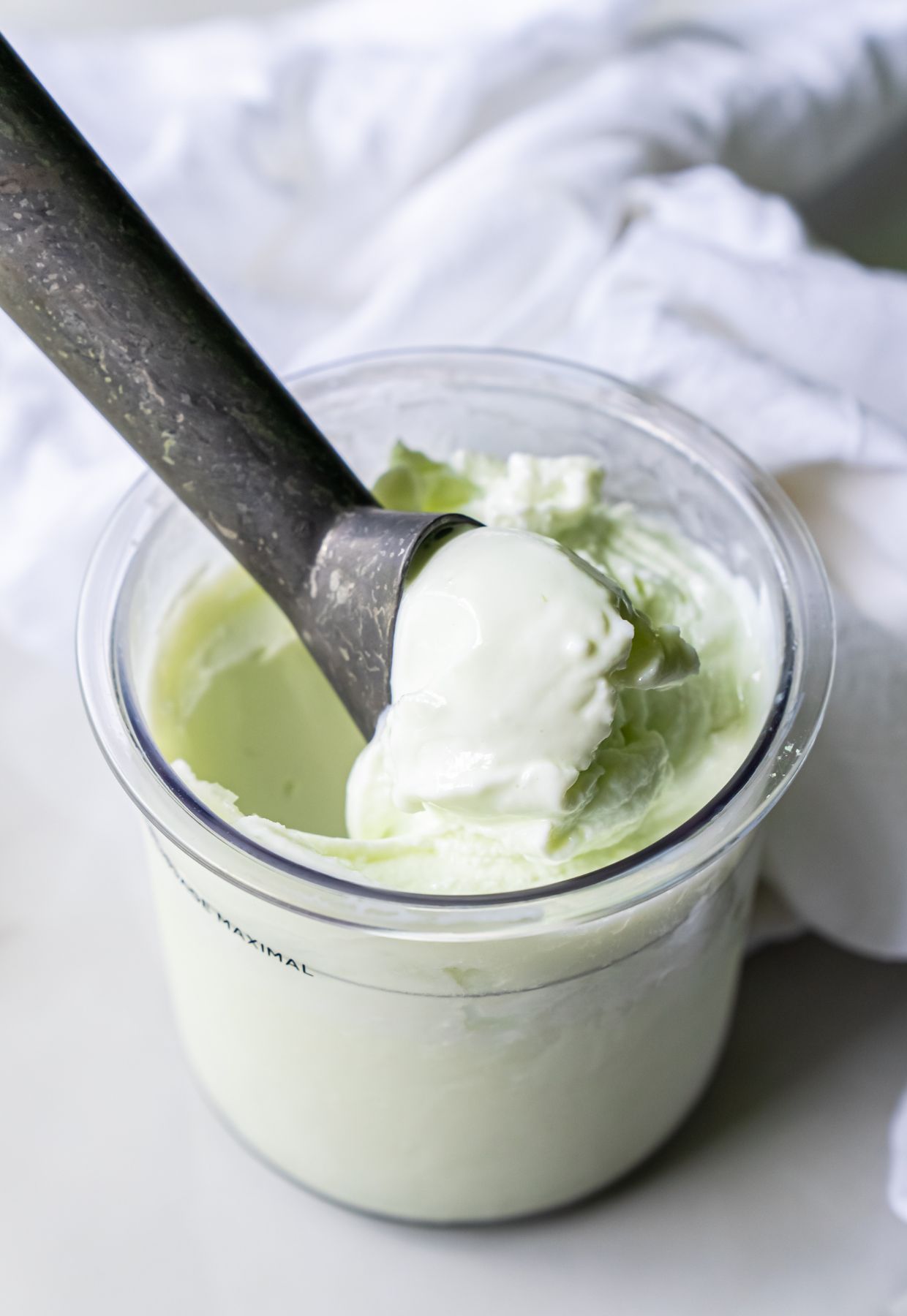 A scoop of light green ice cream is being taken from a container with a metal ice cream scooper, adding a delightful touch to the world of desserts.