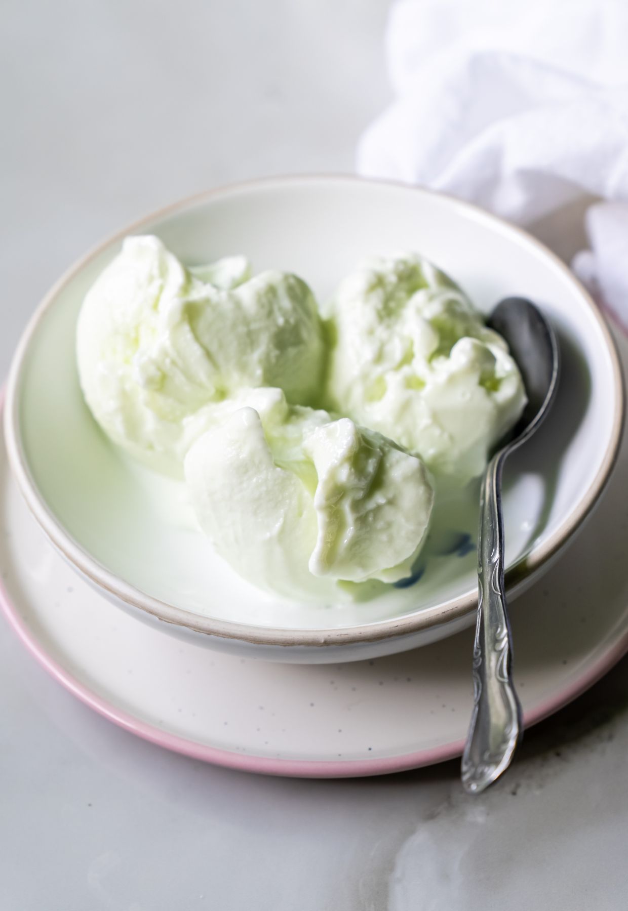 A bowl with three scoops of light green ice cream, a metal spoon, and a stack of two plates—a delightful dessert presentation.