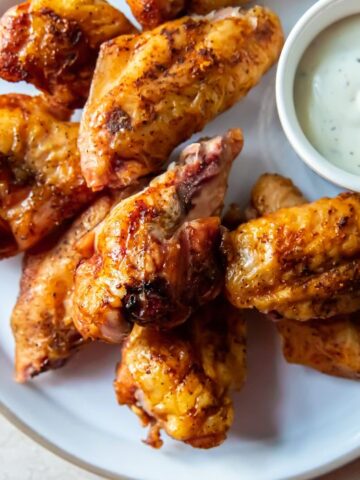 A plate of grilled chicken wings with a side of creamy white dipping sauce makes for perfect snacks.