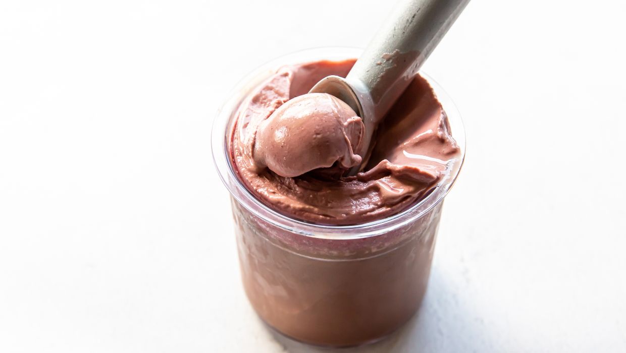A spoon scooping chocolate pudding from a glass jar on a white surface.