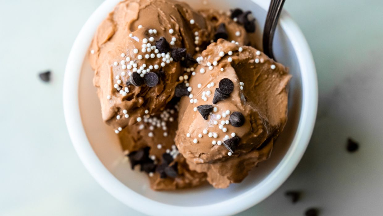 A bowl of chocolate ice cream topped with chocolate chips and white sprinkles, served with a spoon, makes for one of the most delightful desserts.