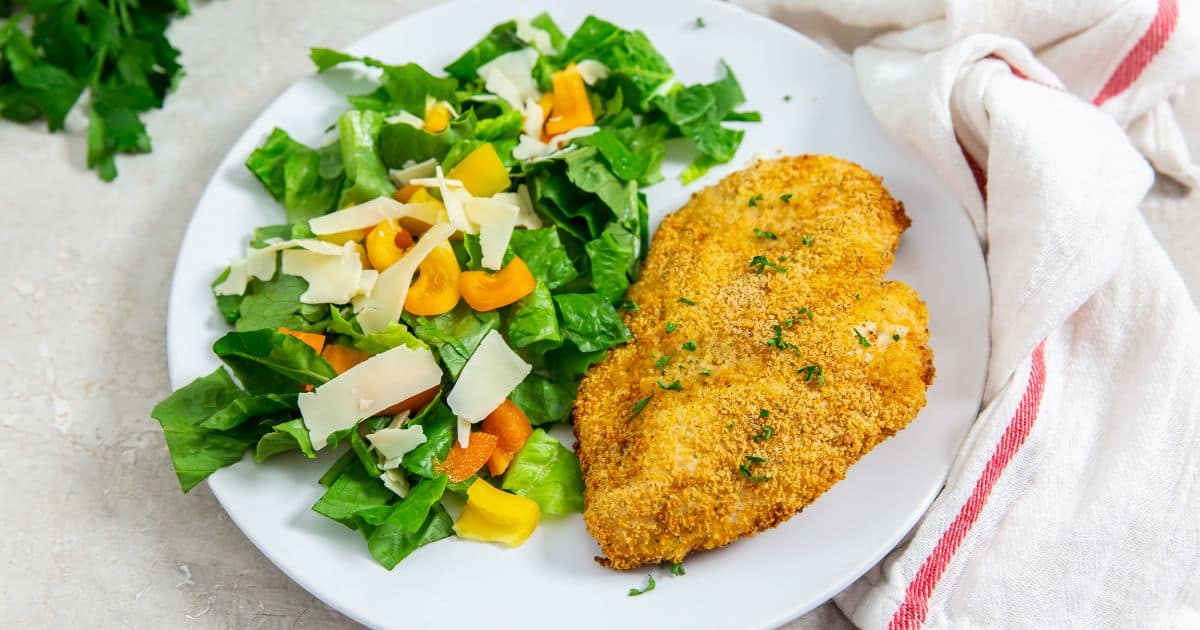 Easy Air Fryer Shake n Bake Chicken Breast on a white plate with a salad topped with bell peppers and parmesan.