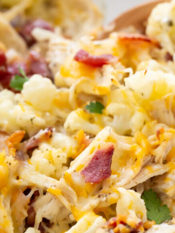 Cheesy chicken and bacon pasta in a creamy sauce, garnished with herbs, served in a white bowl with a wooden spoon.