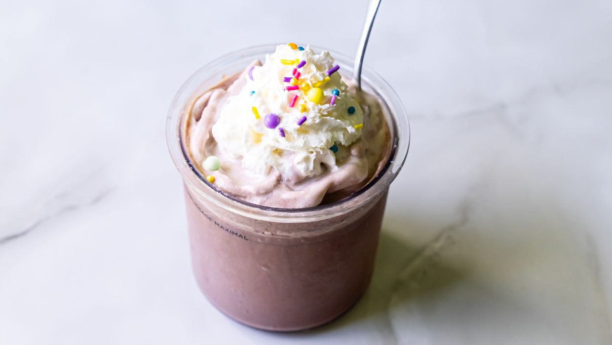 A chocolate milkshake topped with whipped cream and colorful sprinkles, in a clear plastic cup with a spoon—one of the 10 low-carb sweet treats you'll love.