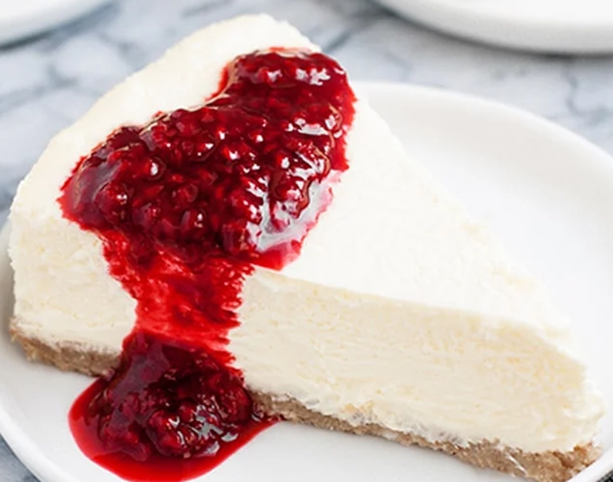 A slice of cheesecake topped with raspberry sauce on a white plate, one of 12 low carb desserts you'll love.