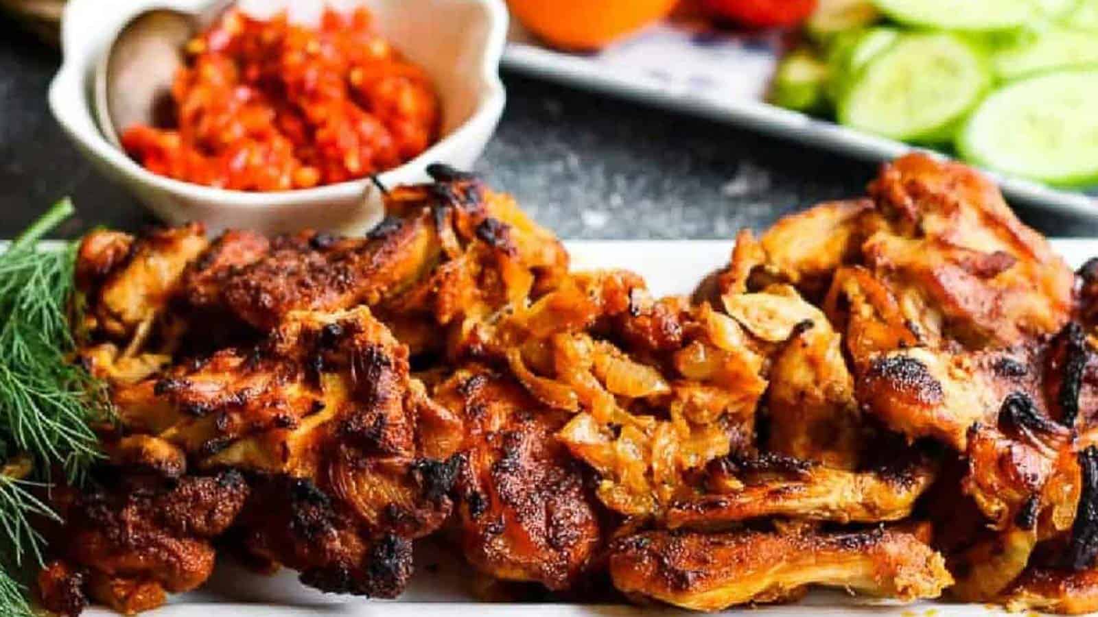 Low angle shot of chicken shawarma on a white platter with harissa paste and tomatoes and cucumbers in the background.