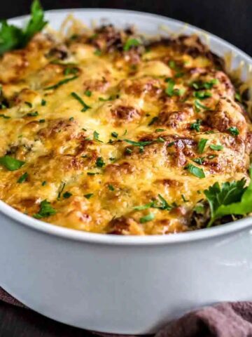 A baked casserole dish filled with a cheesy, golden-brown lasagna garnished with fresh parsley leaves, just one of the 21 addictive casseroles you need to try.