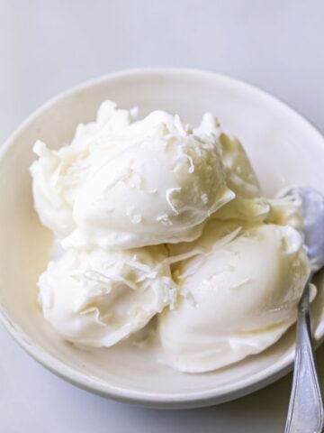 A bowl containing four scoops of white ice cream with a spoon placed inside.