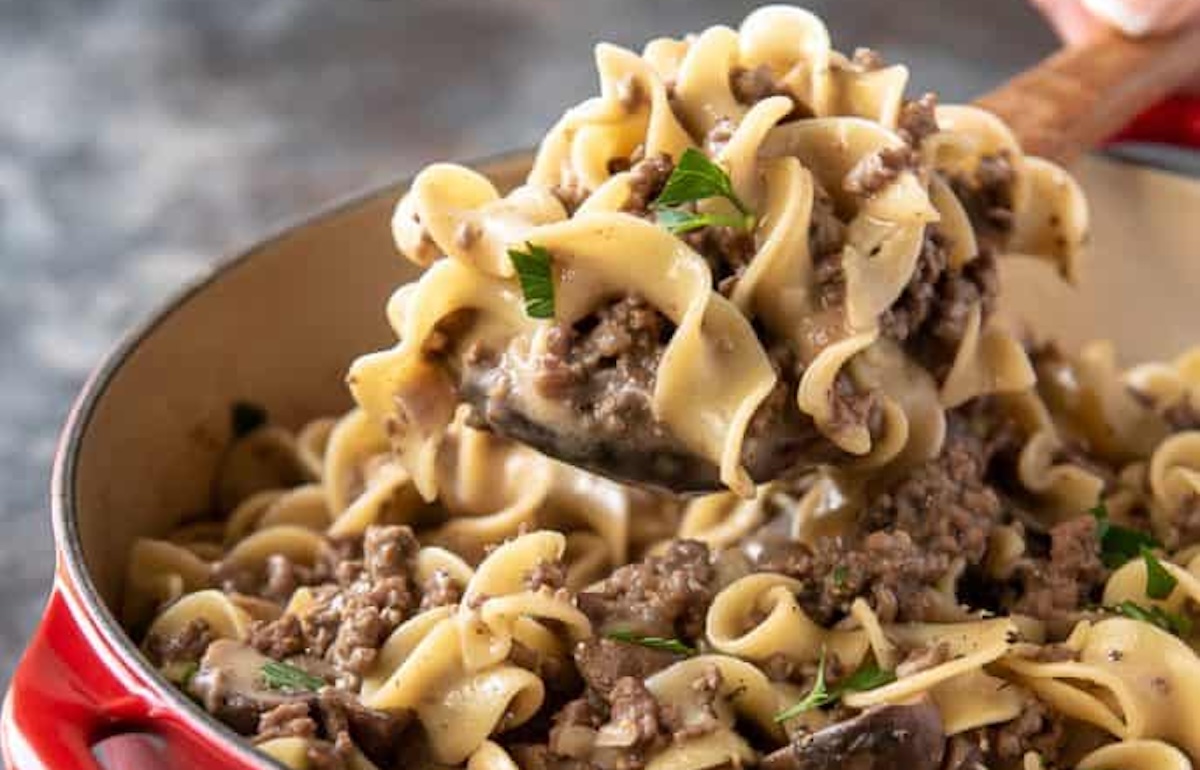 A close-up of a pot of beef stroganoff with wide egg noodles being scooped by a spoon, showcasing one of our 14 easy dinner recipes. The dish is garnished with parsley.