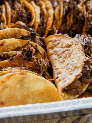 A tray filled with numerous folded tacos, each containing shredded beef from one of our 20 beef recipes.