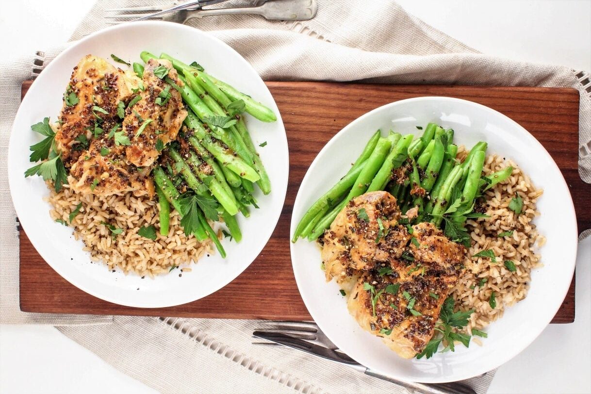 Two plates of chicken with herbs served over rice and asparagus on a wooden board, reminiscent of the flavors found in 17 chicken instant pot recipes.