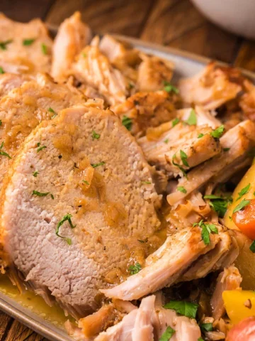 A plate of sliced roast pork, garnished with herbs, served with roasted potatoes and carrots—perfect for fans of 31 sneaky recipes that make dinner extraordinary.