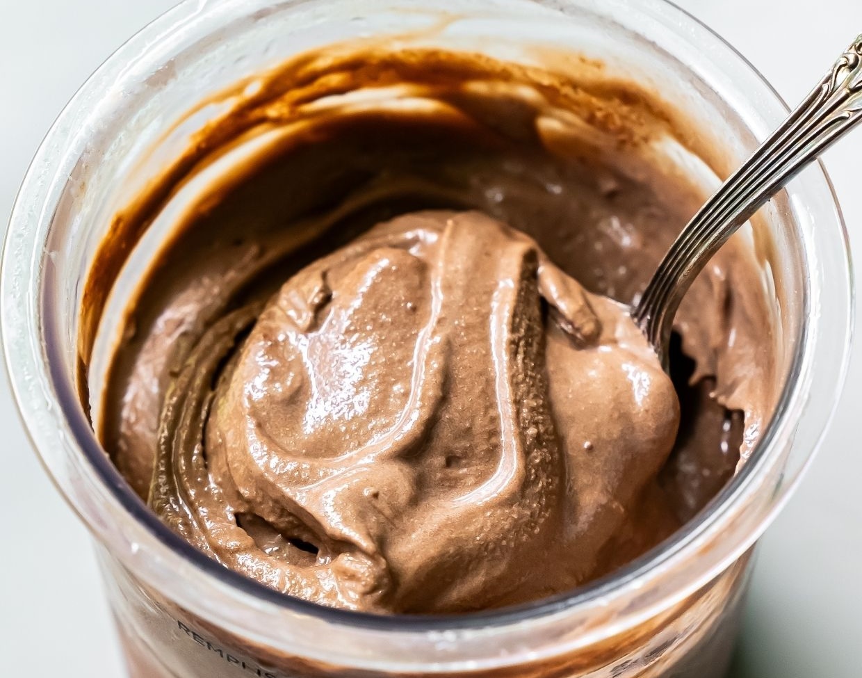 A close-up view of creamy chocolate ice cream in a clear container with a spoon inside, reminiscent of the indulgence found in 10 Ninja Creami ice creams.