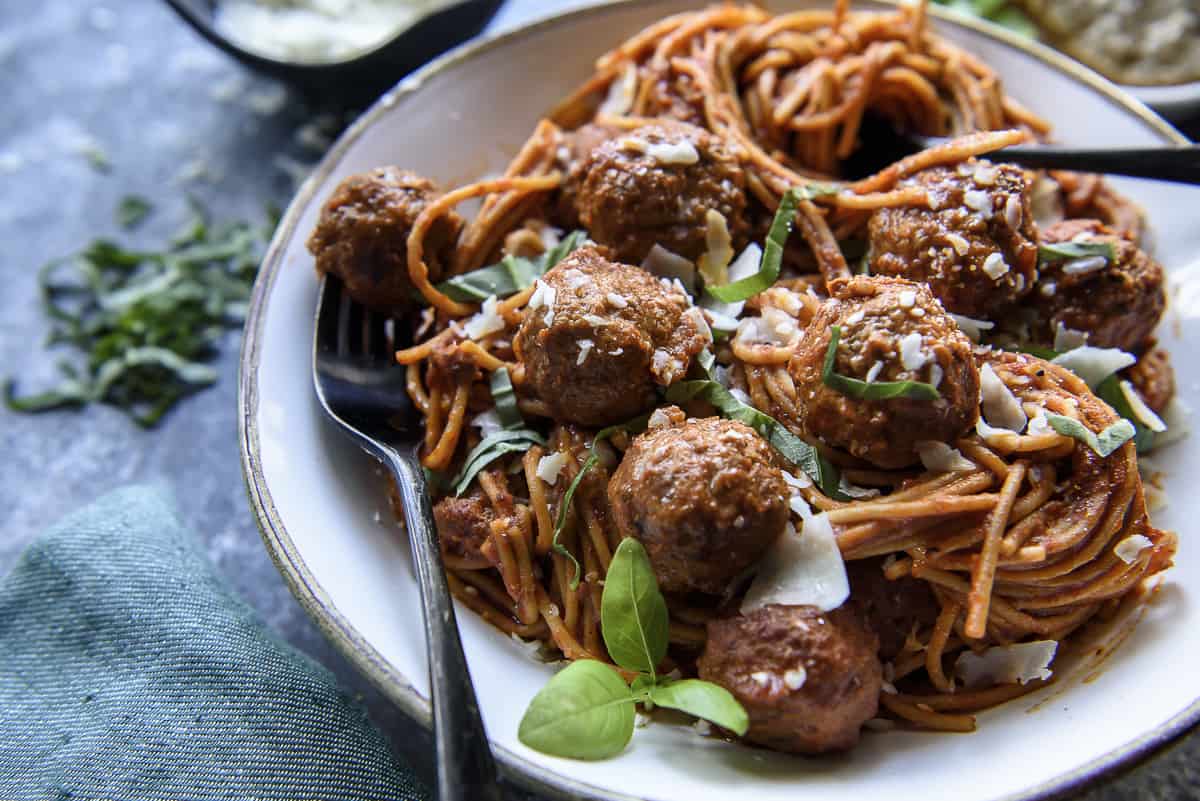 A plate of spaghetti topped with meatballs, shredded cheese, and fresh basil, with a fork placed in the bowl—perfect for your next dinner idea.
