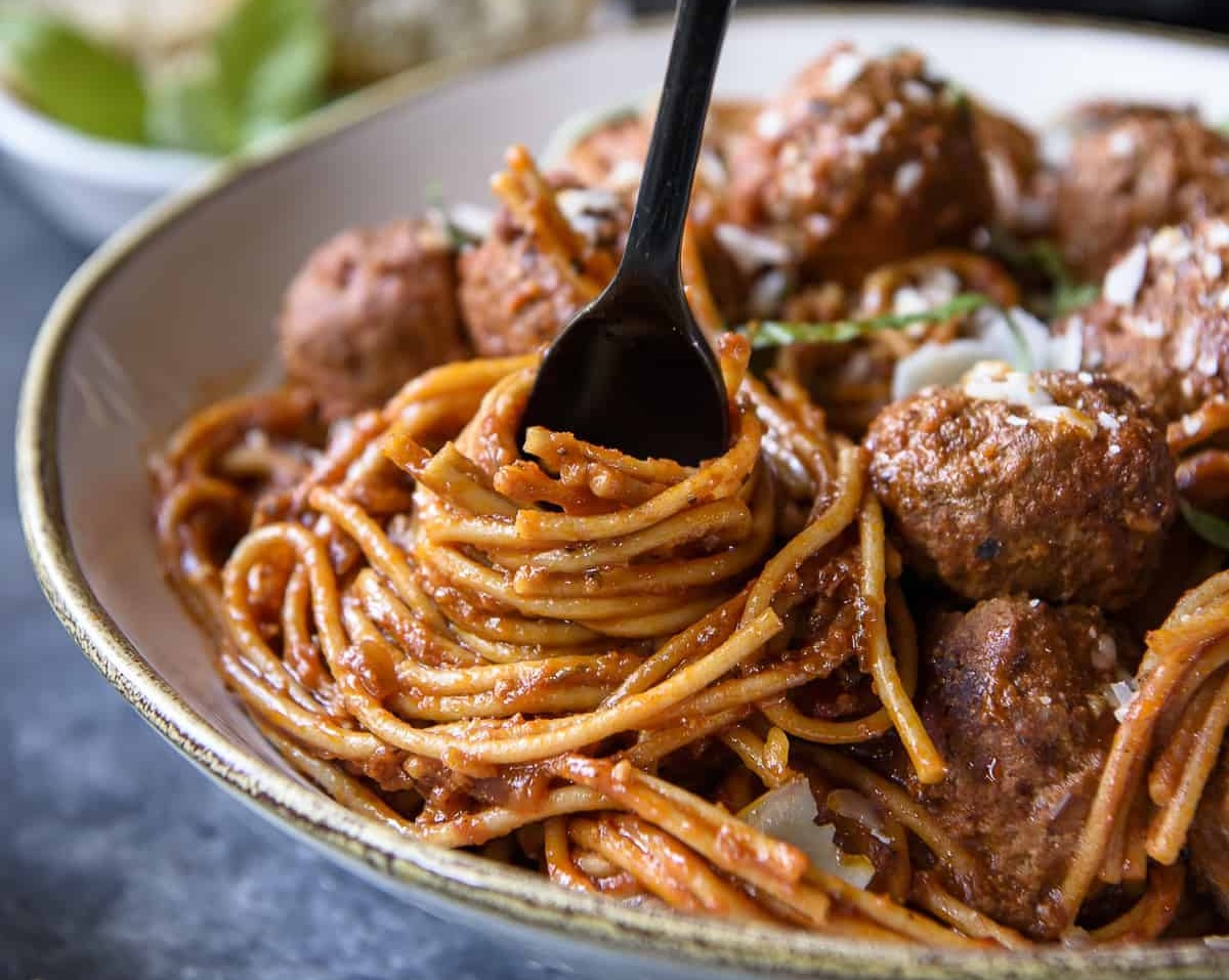 A bowl of spaghetti with tomato sauce and meatballs, topped with grated cheese. A black fork is twirling the spaghetti, making it one of the perfect dinner ideas.