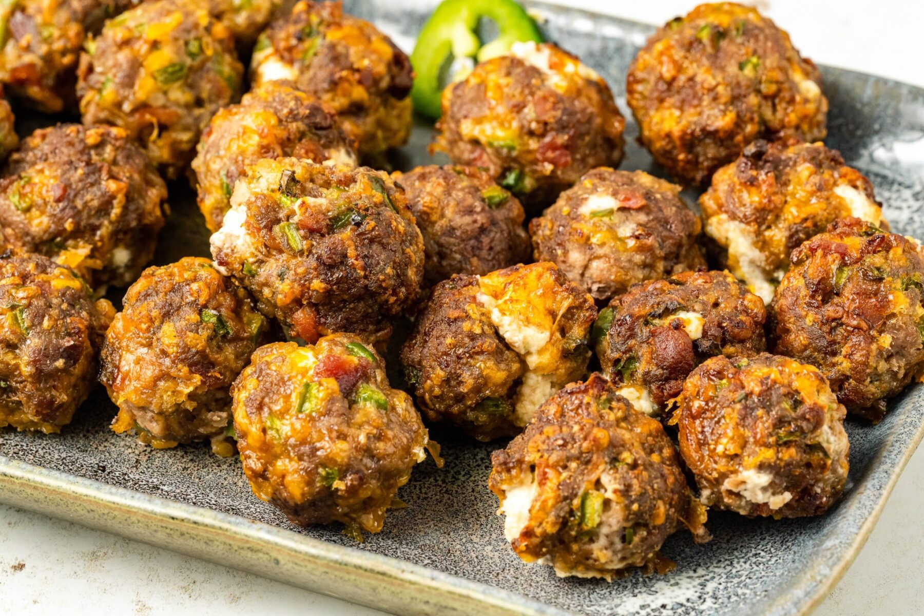 A plate of browned meatballs garnished with herbs and spices, featuring a slice of green pepper in the background—perfect for those seeking inspiring meatball recipes.