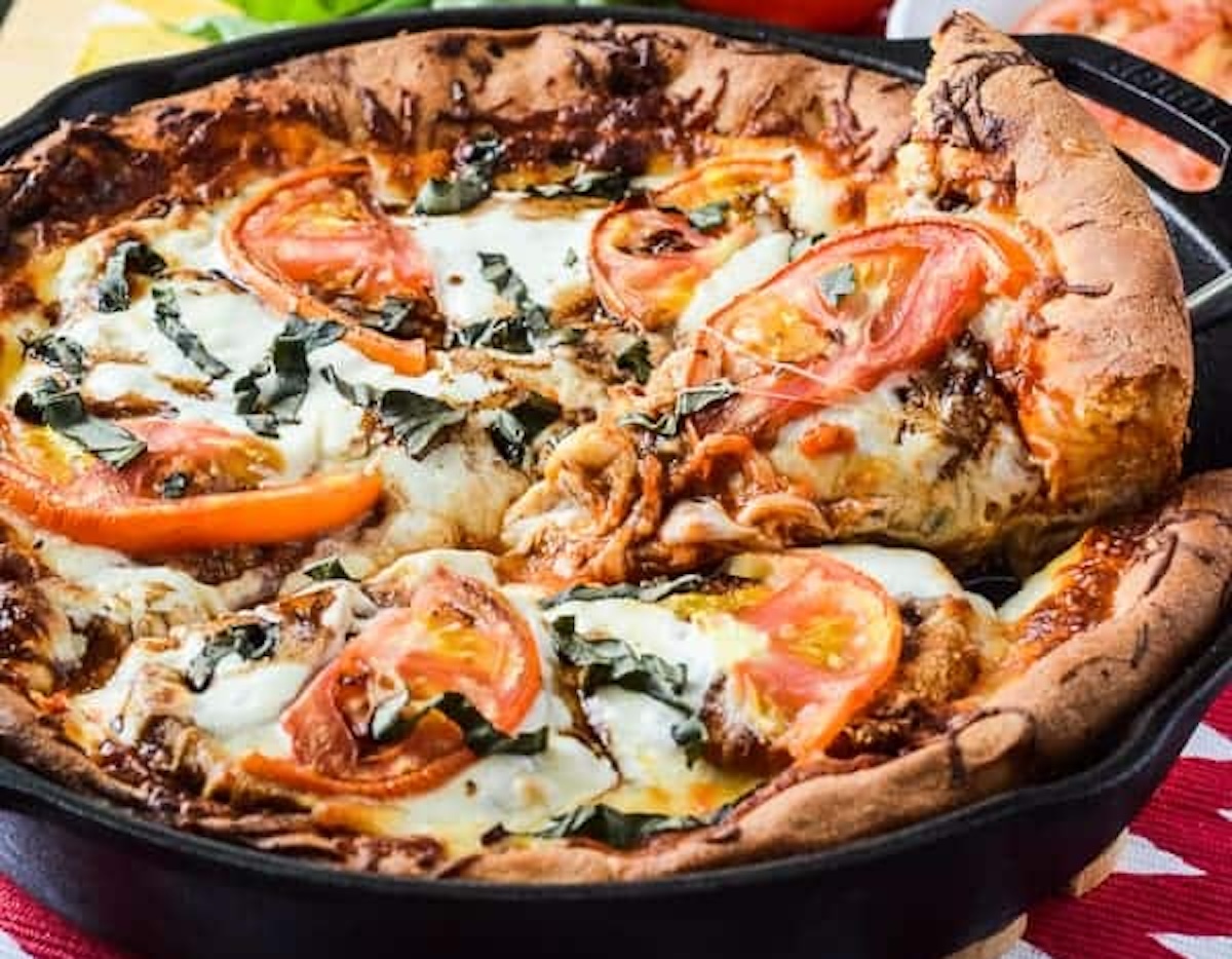A freshly baked deep-dish pizza with melted cheese, tomato slices, and basil leaves in a cast-iron skillet is one of the 23 skillet dinners that bring comfort and flavor to your table.