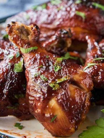 Close-up of a plate with several pieces of glazed, grilled chicken garnished with chopped herbs. Perfect for those looking to try an irresistible chicken recipe.