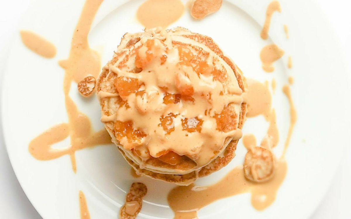 A stack of pancakes topped with syrup and small pieces of fruit on a white plate, with additional drizzles of syrup around the plate, makes for one of the top 20 breakfasts to start your day.