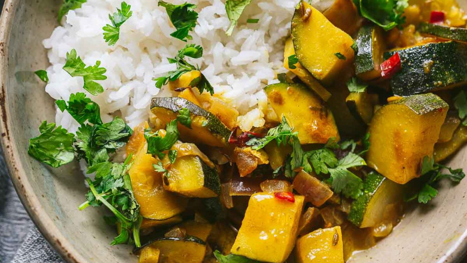 A bowl of rice served with a vegetable curry containing zucchini, cilantro, and spices.