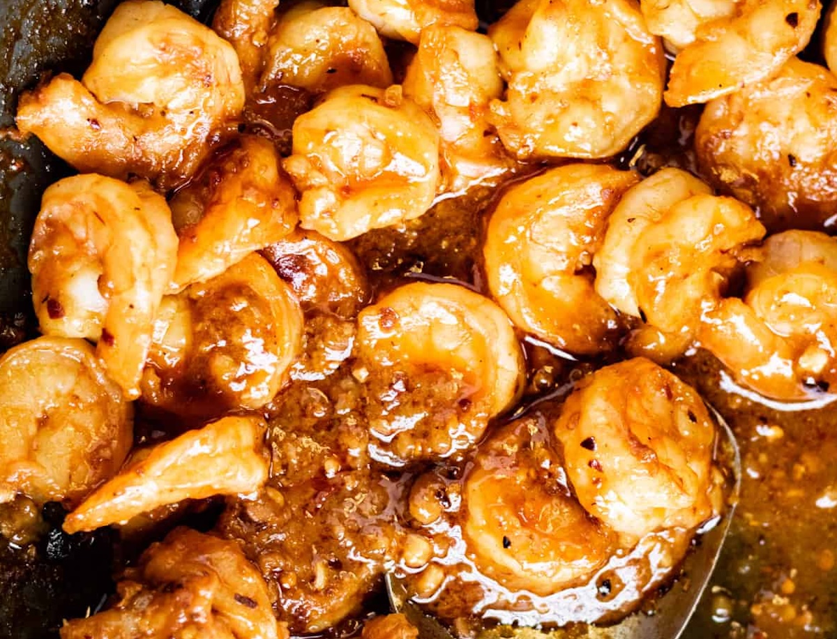 Close-up of cooked shrimp dishes in a glistening, savory sauce with visible herbs and spices.