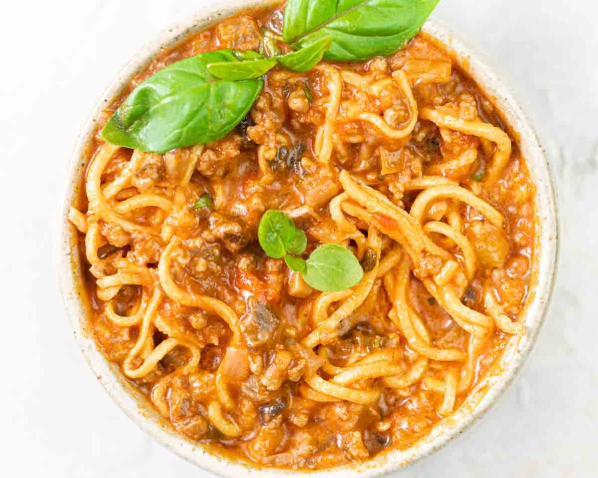 A delicious meal, this bowl of spaghetti bolognese is garnished with fresh basil leaves on top.
