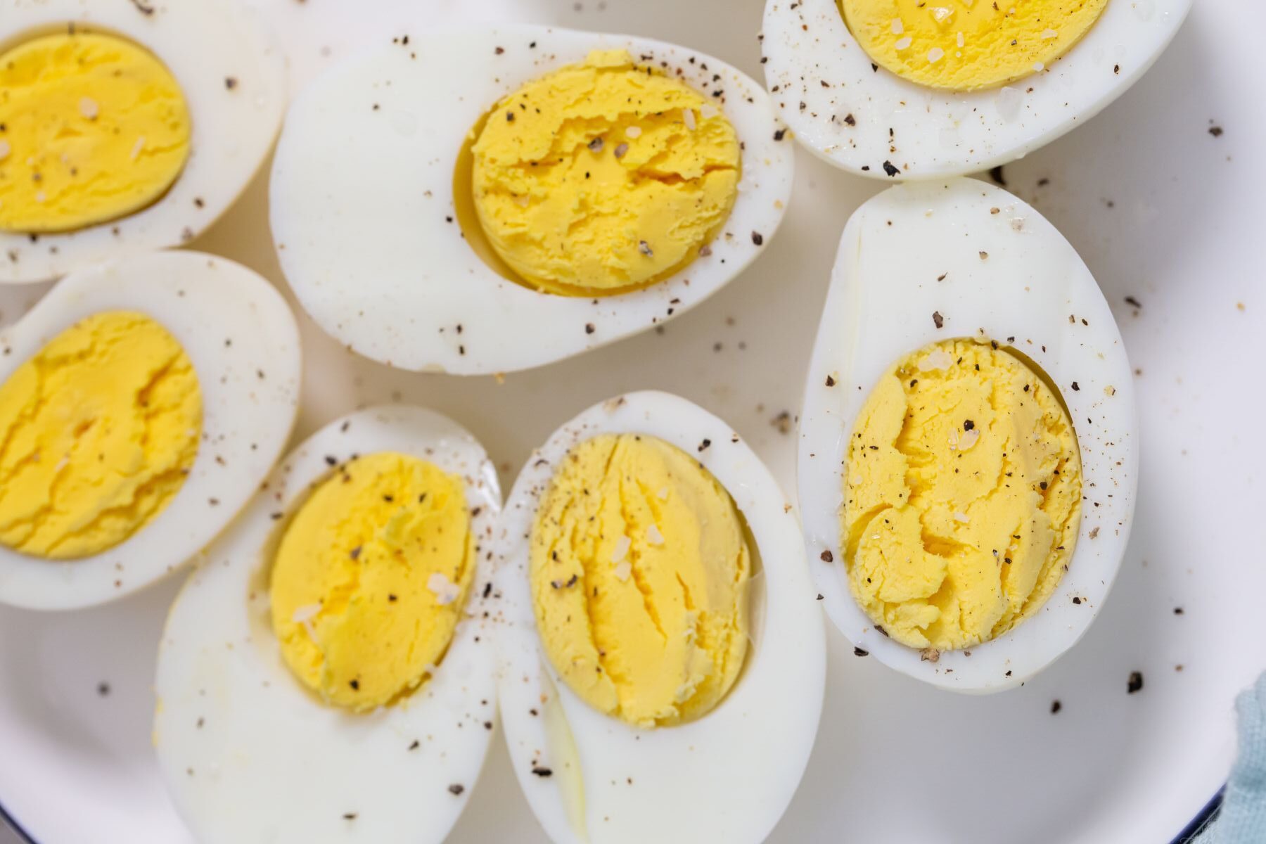 Close-up of halved hard-boiled eggs, sprinkled with salt and pepper, served on a white plate.
