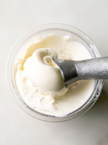 A metal scoop is scooping out vanilla ice cream from a clear container.