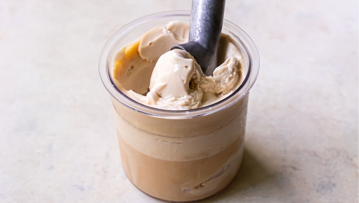 A cup of light brown ice cream with a scoop inserted, sitting on a light-colored surface, ready to join your lineup of 10 Ninja Creami ice creams.