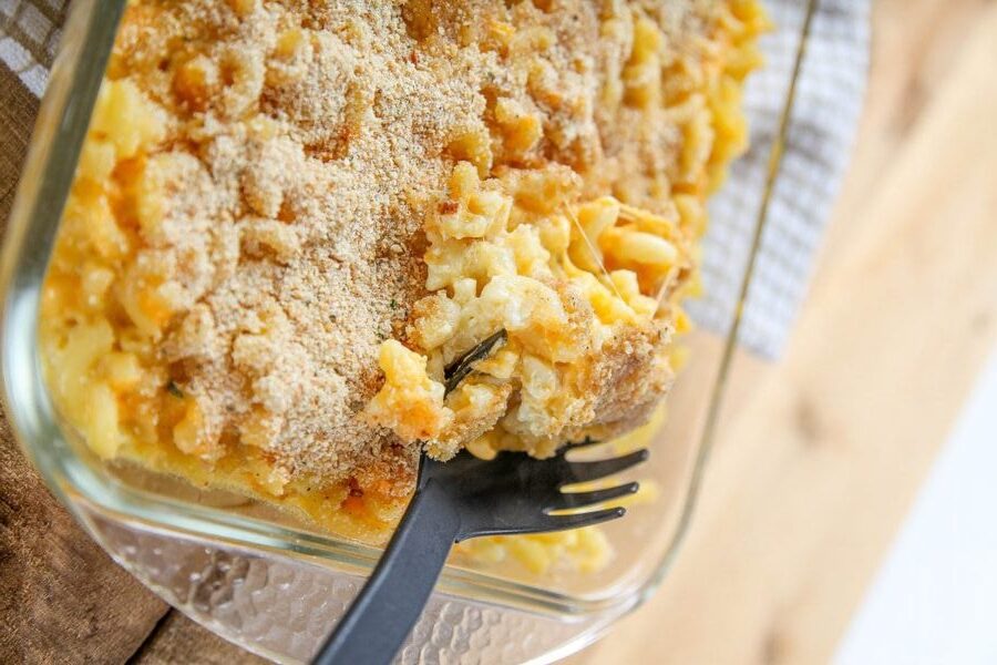 A close-up of baked macaroni and cheese in a glass dish with a black serving spoon.