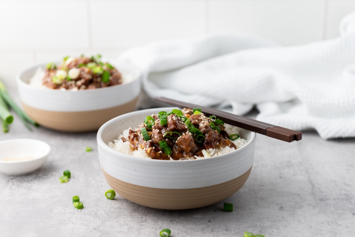Two bowls of rice topped with stir-fried beef and green onions, with chopsticks resting on one bowl.