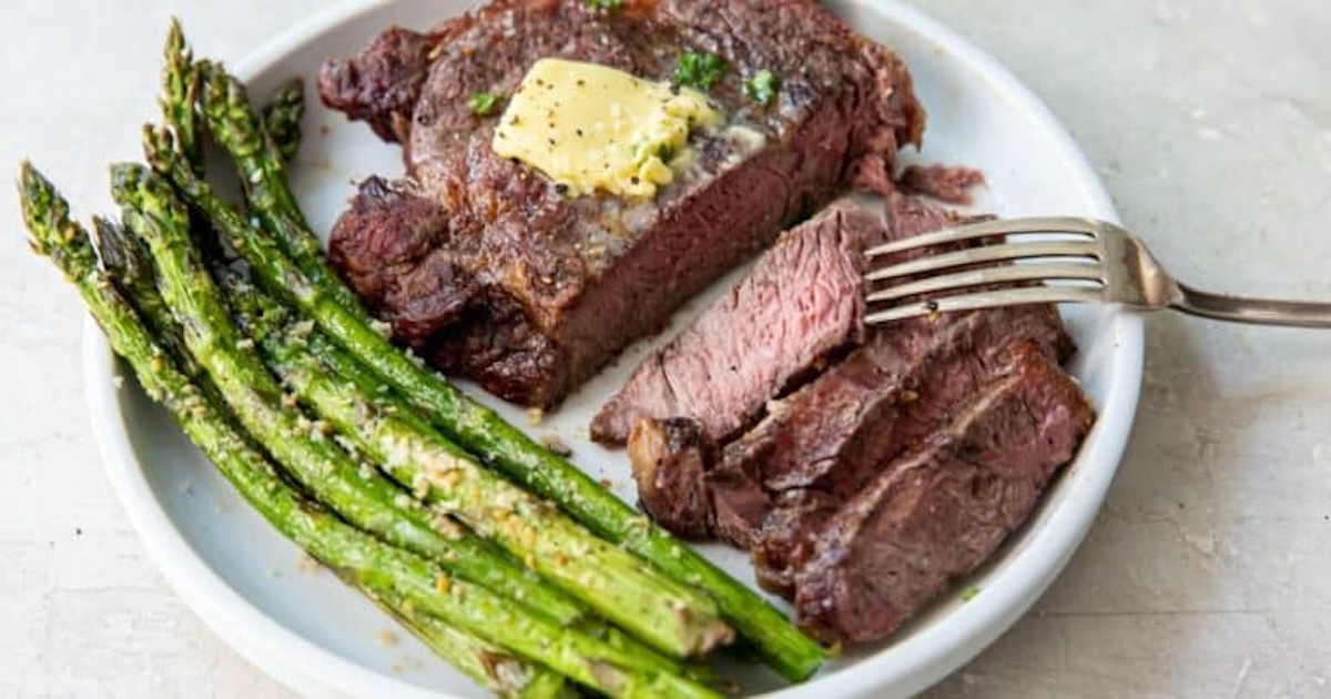 A plate with sliced steak topped with herb butter and a side of cooked asparagus.