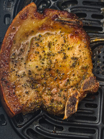 Close-up of a cooked steak with seasoning, sitting on a black grill surface.