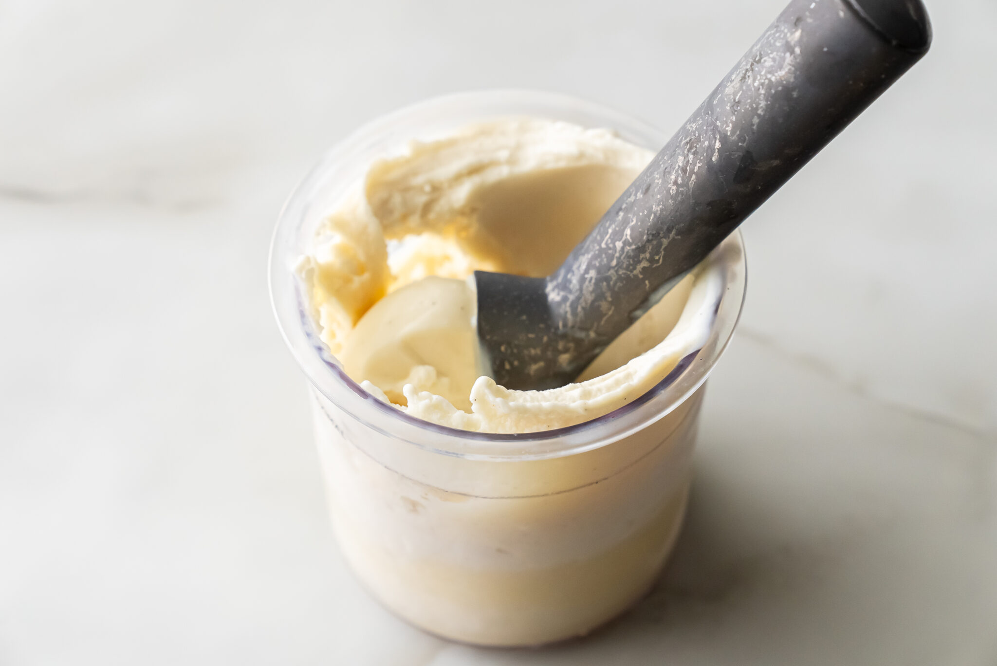 The Best Ninja Creami Vanilla Protein Ice Cream Recipe (Without Pudding Mix or Cream Cheese) in a transparent container with a scooper.